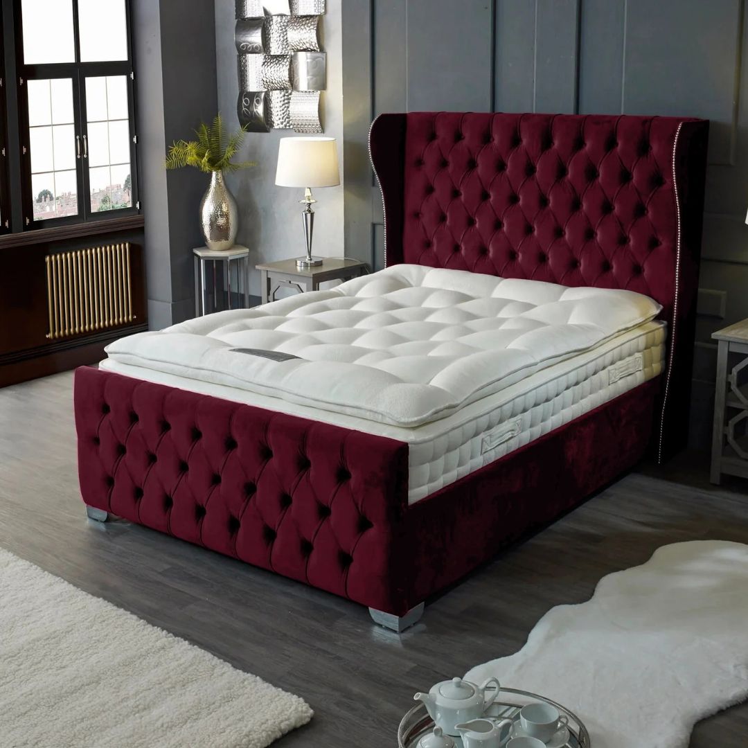 Maroon tufted bed frame with white mattress in a bedroom setting.